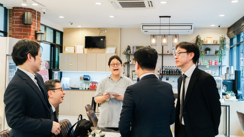 A staff member with a disability from the APCD 60+ Plus Bakery & Chocolate Project takes orders from the JICA representatives.