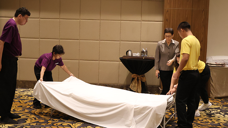 ภาพที่ 4: ผู้เข้าอบรมใส่เสื้อสีม่วง 2 คน (ซ้าย) และผู้เข้าอบรมใส่เสื้อสีเหลือง (ขวา) สาธิตวิธีการปูเตียง