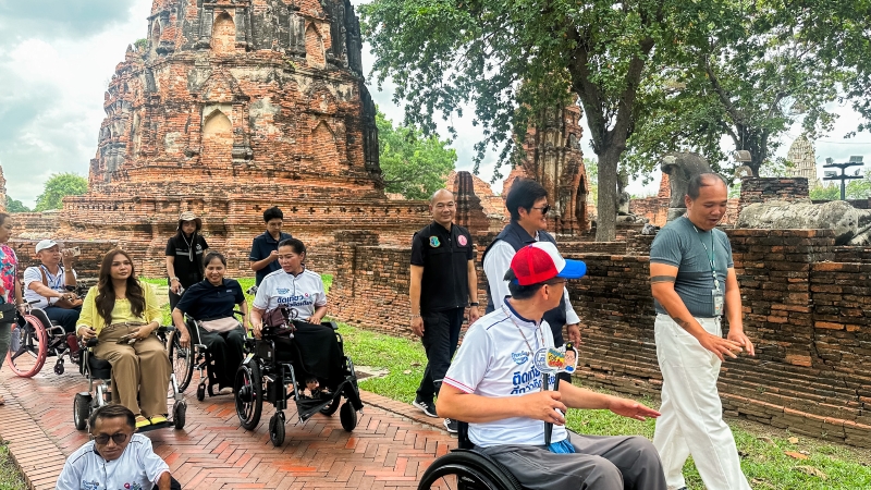 Picture 5: Participants in wheelchairs tour the site in Phra Nakhon Si Ayutthaya while the docent provides information, with a pagoda in the background