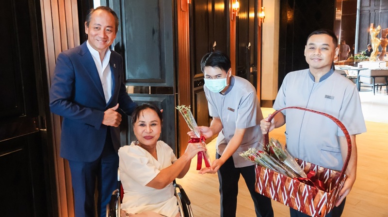 Picture 5: From left to right, Mr. Sammy Carolus, Ms. Nongnuch Maytarjittipun (seated in a wheelchair) and a male trainee, both holding a rose together, and a male trainee holds a bucket of roses