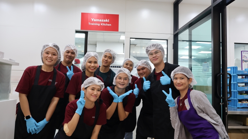 Representatives from Canopy by Hilton Bangkok Sukhumvit hold a 'Travel with Purpose' sign while posing for a photo before a bakery workshop session.