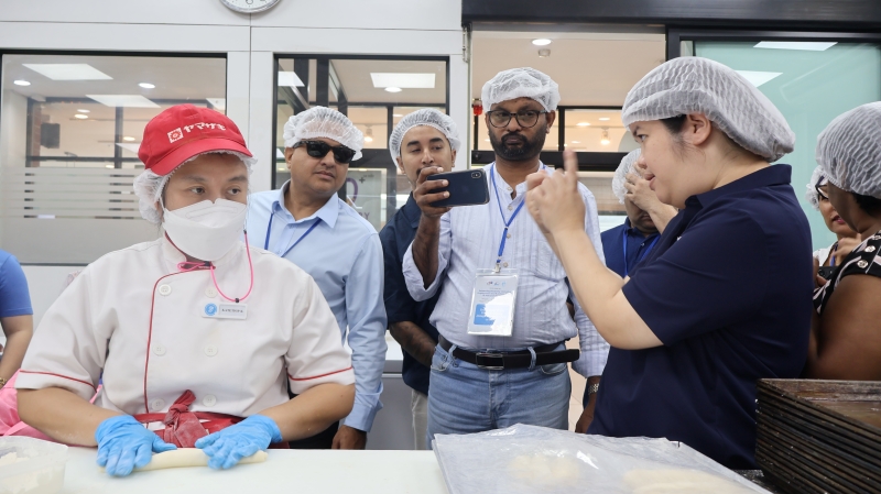 Ms. Supaanong Panyasirimongkol guided the visit as participants observed employees with disabilities performing bakery production tasks and learned about inclusive workplace practices.