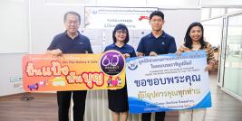 Picture 1: A group photo featuring Mr. Piroon Laismit, Executive Director of APCD (far left), and representatives from the Bangkok School for the Blind (center) holding a "Pun Pang, Pun Boon" campaign sign, alongside Ms. Wilailekha Somprach, Manager of APCD 60+ Plus Projects (far right), holding a thank-you sign, with boxes of bread stacked in the background.