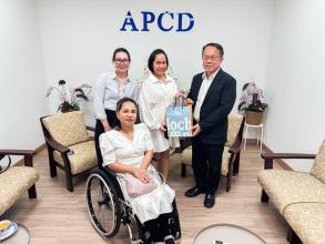 Picture 1: From left to right, Ms. Nitwari Sikon, Ms. Kingkarn Siriwat (left) and Mr. Piroon Laismit (right), both holding a gift together and Ms. Nongnuch Maytarjittipun (seated in a wheelchair in front of Ms. Nitwari Sikon)
